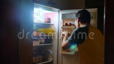 人们晚上从冰箱里吃饥饿和<strong>饕餮</strong>。 男人晚上看冰箱。 生活方式暴食